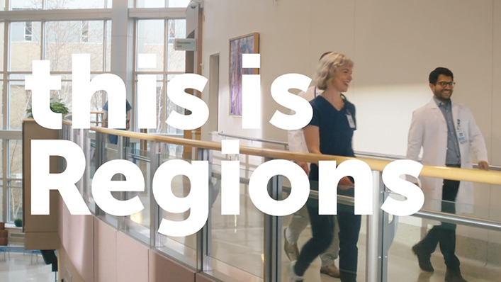 A group of diverse doctors chats as they walk through a hallway full of natural light. The words "this is Regions" is written over the image.